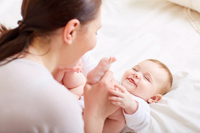 Mother playing with a smiling baby on a bed in a bright and cozy room.