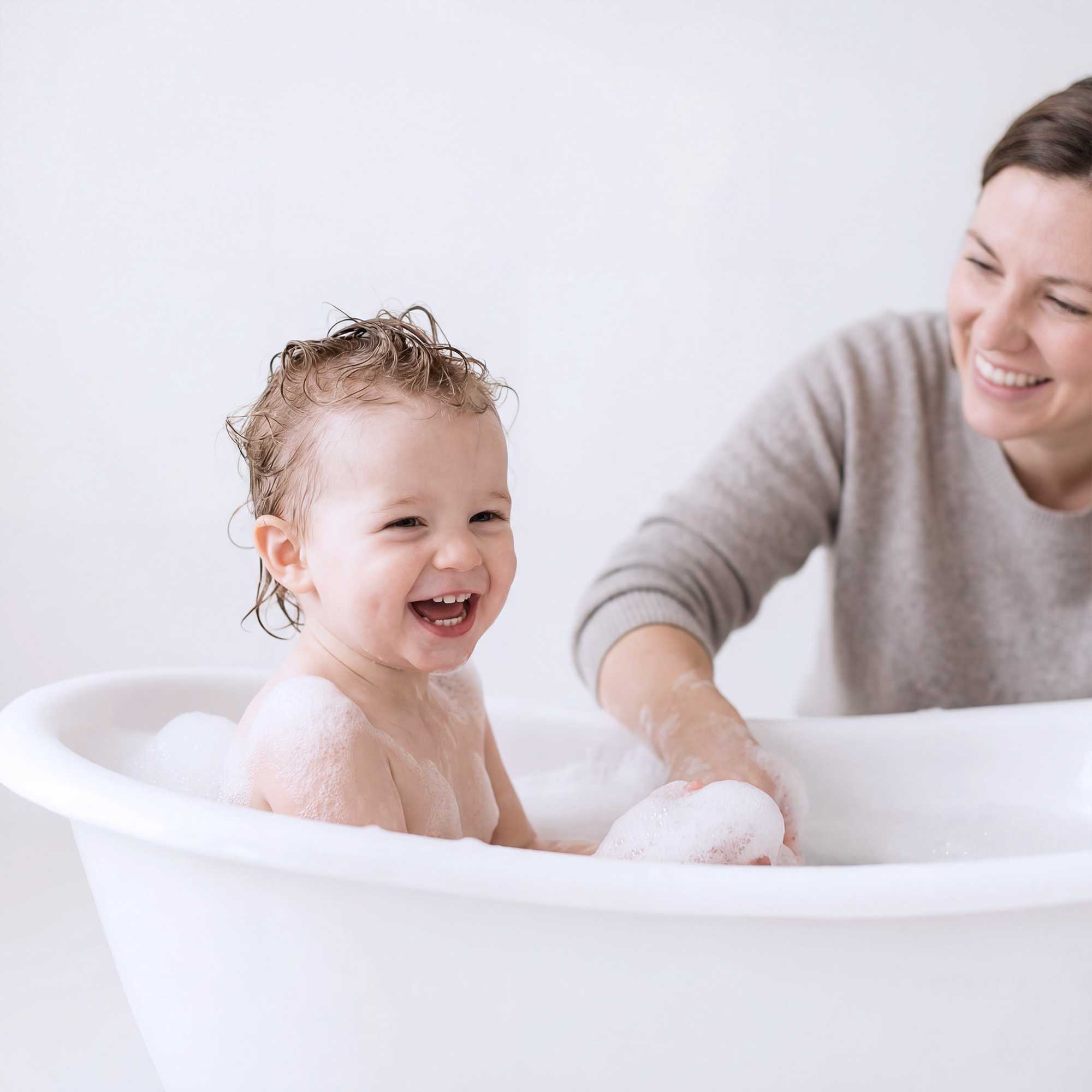 Child in a bathtub with a woman, both smiling, on a light background