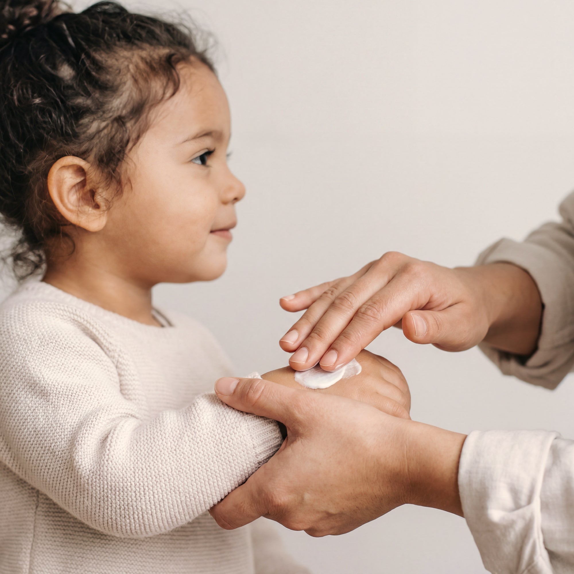 A parent applying cream to her child's hand, cream background