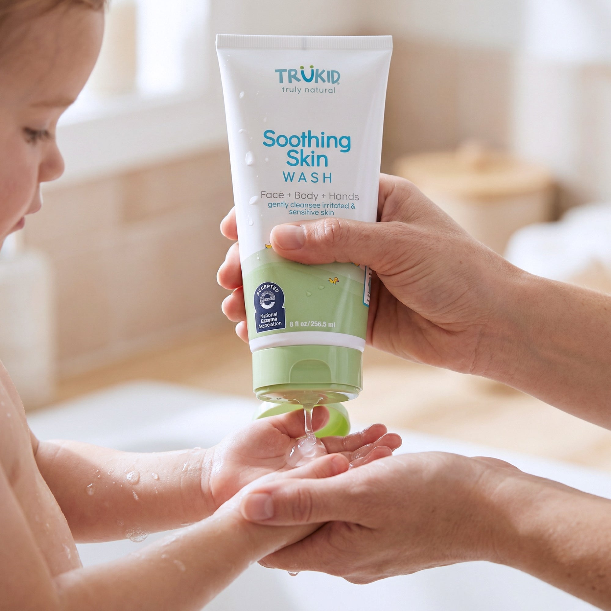Person applying Trukid Soothing Skin Wash to a child's hands in a bathroom setting.