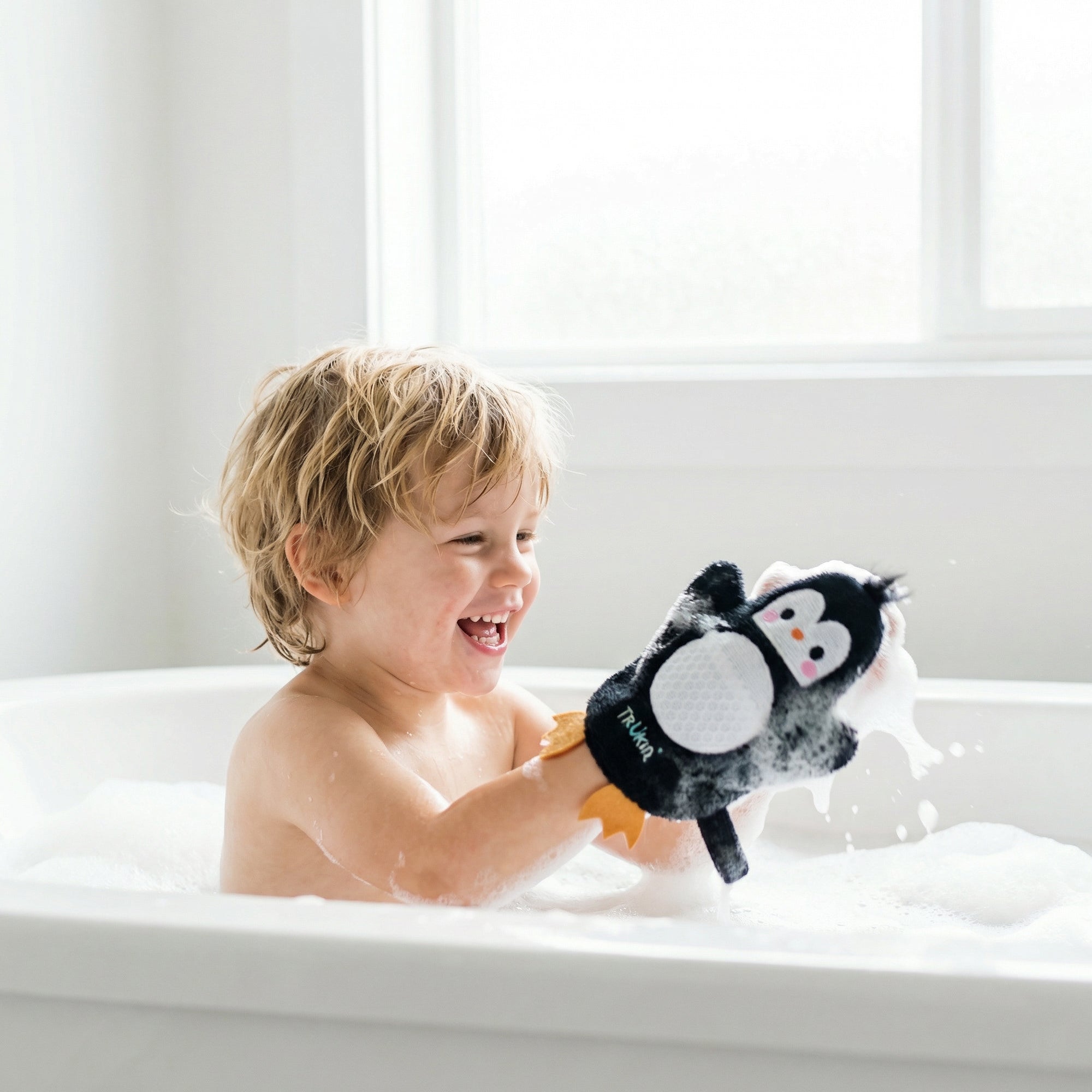 Child in a bathtub holding a penguin shape-bath glove