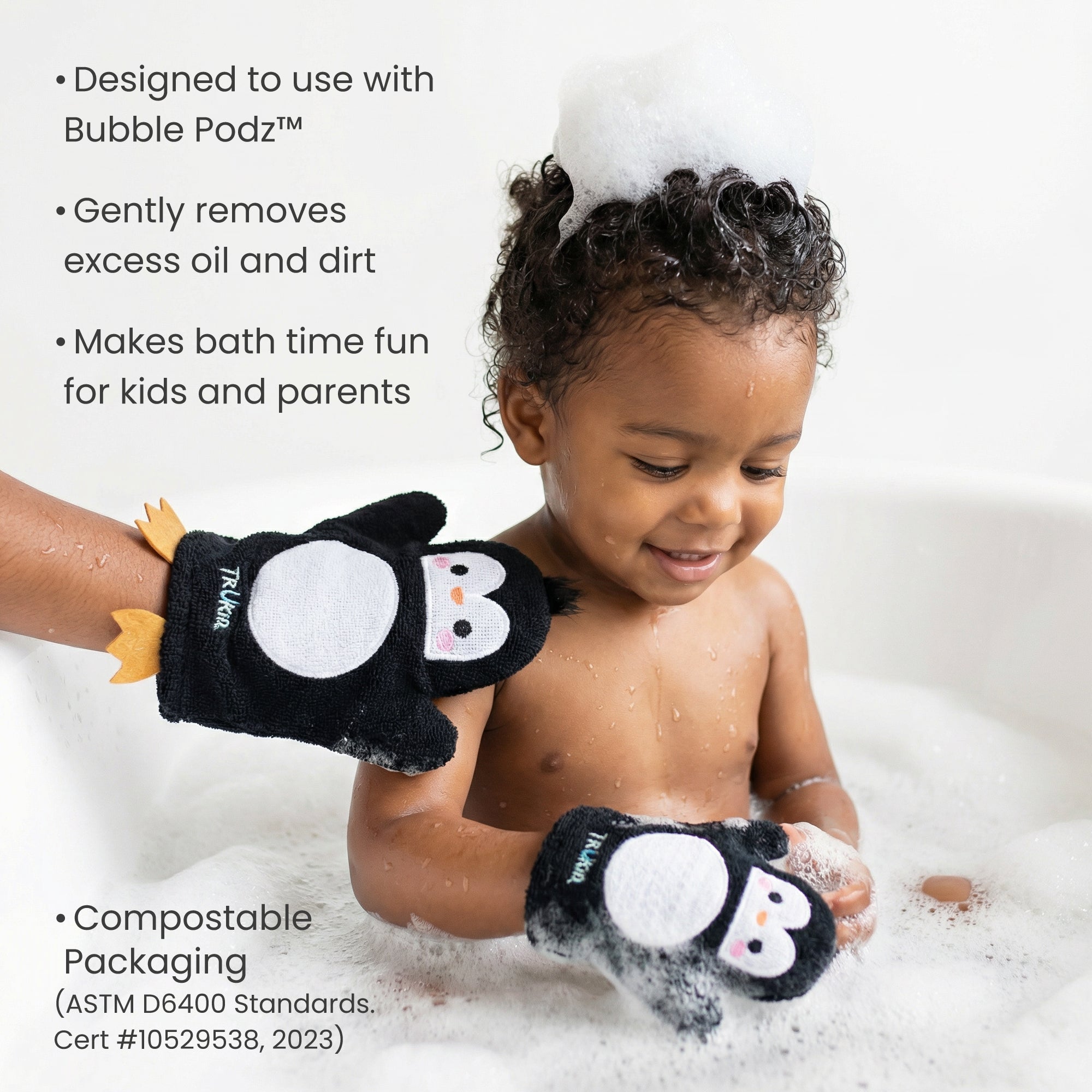 Child in a bath with penguin-themed gloves, surrounded by bubbles.