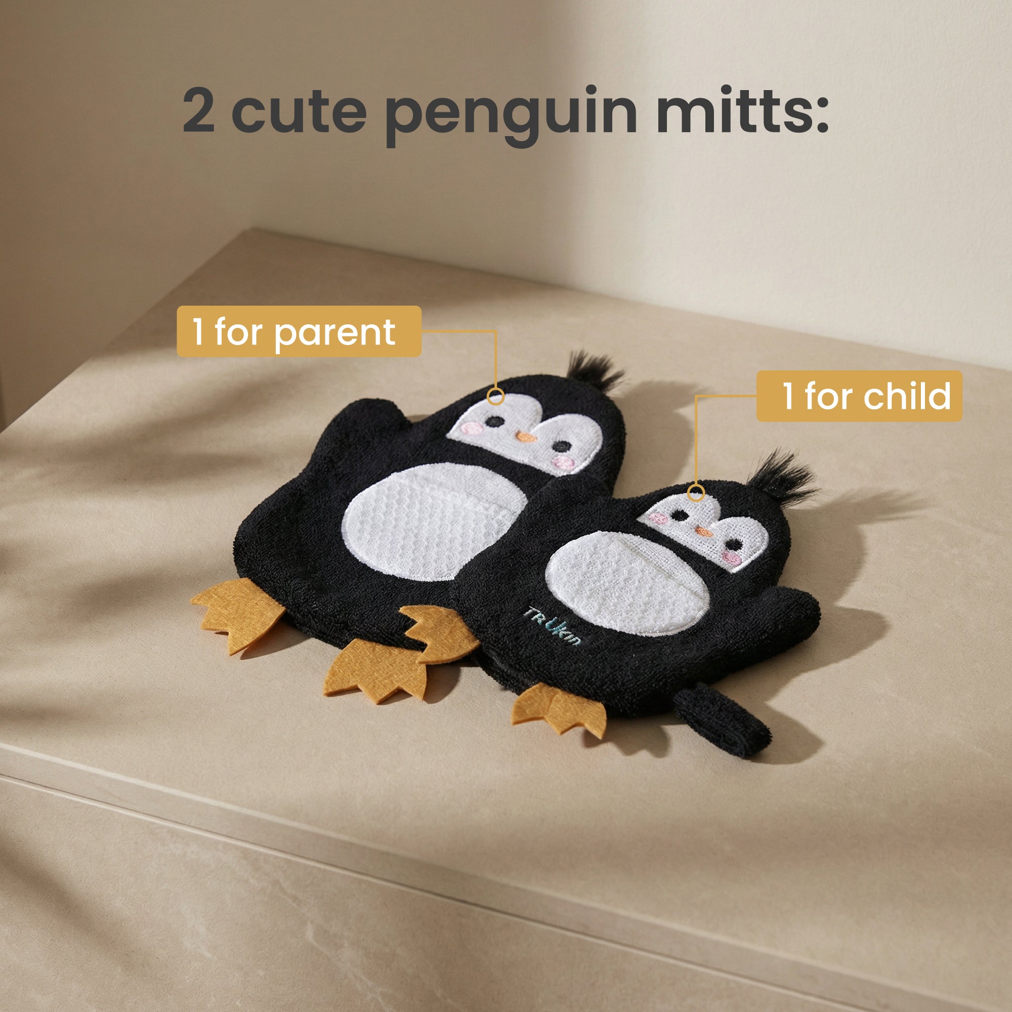 Two penguin mitts for parent and child on a beige surface with text indicating their purpose.