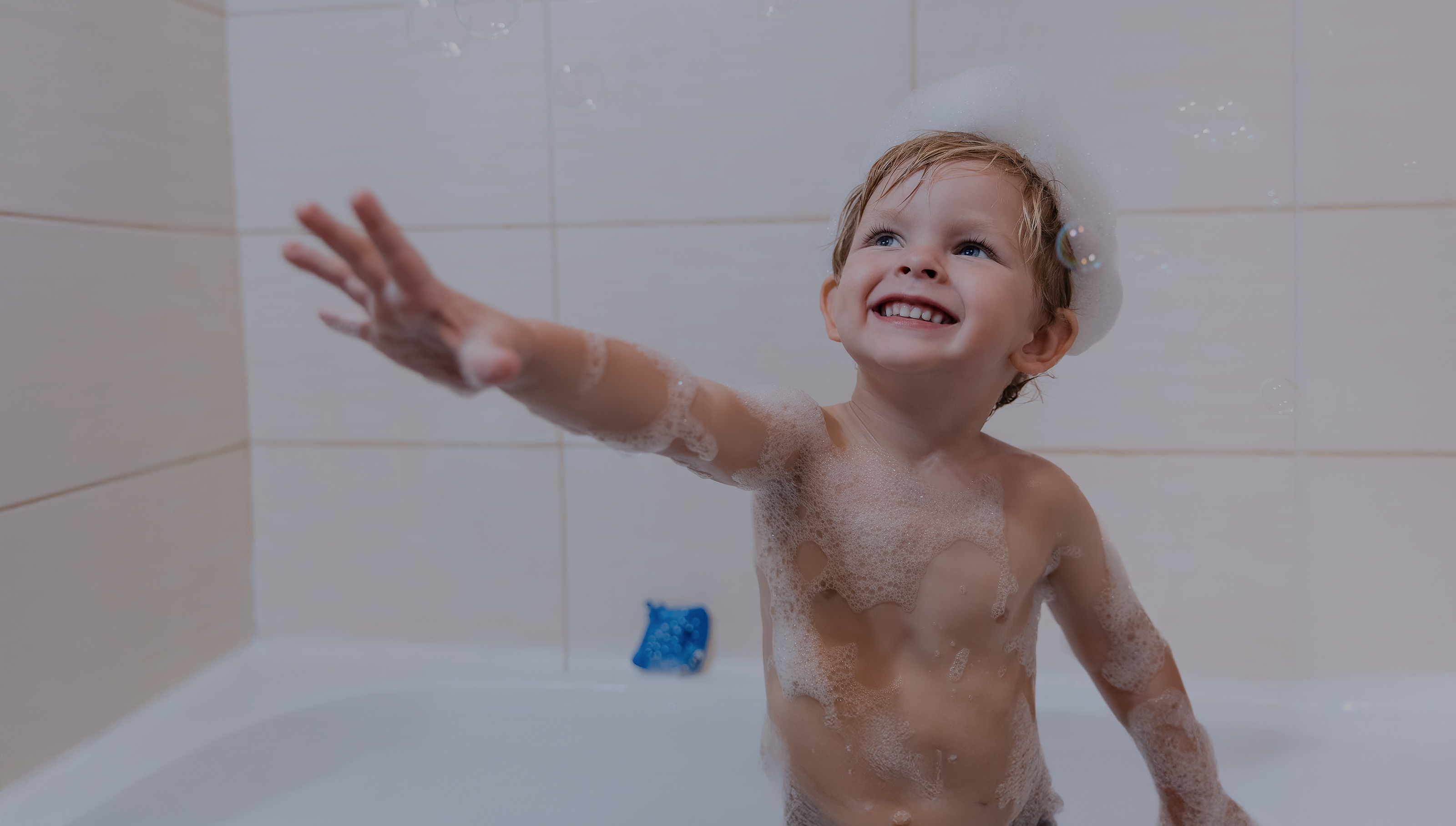 Child taking a bath with soap bubbles in a tiled bathroom